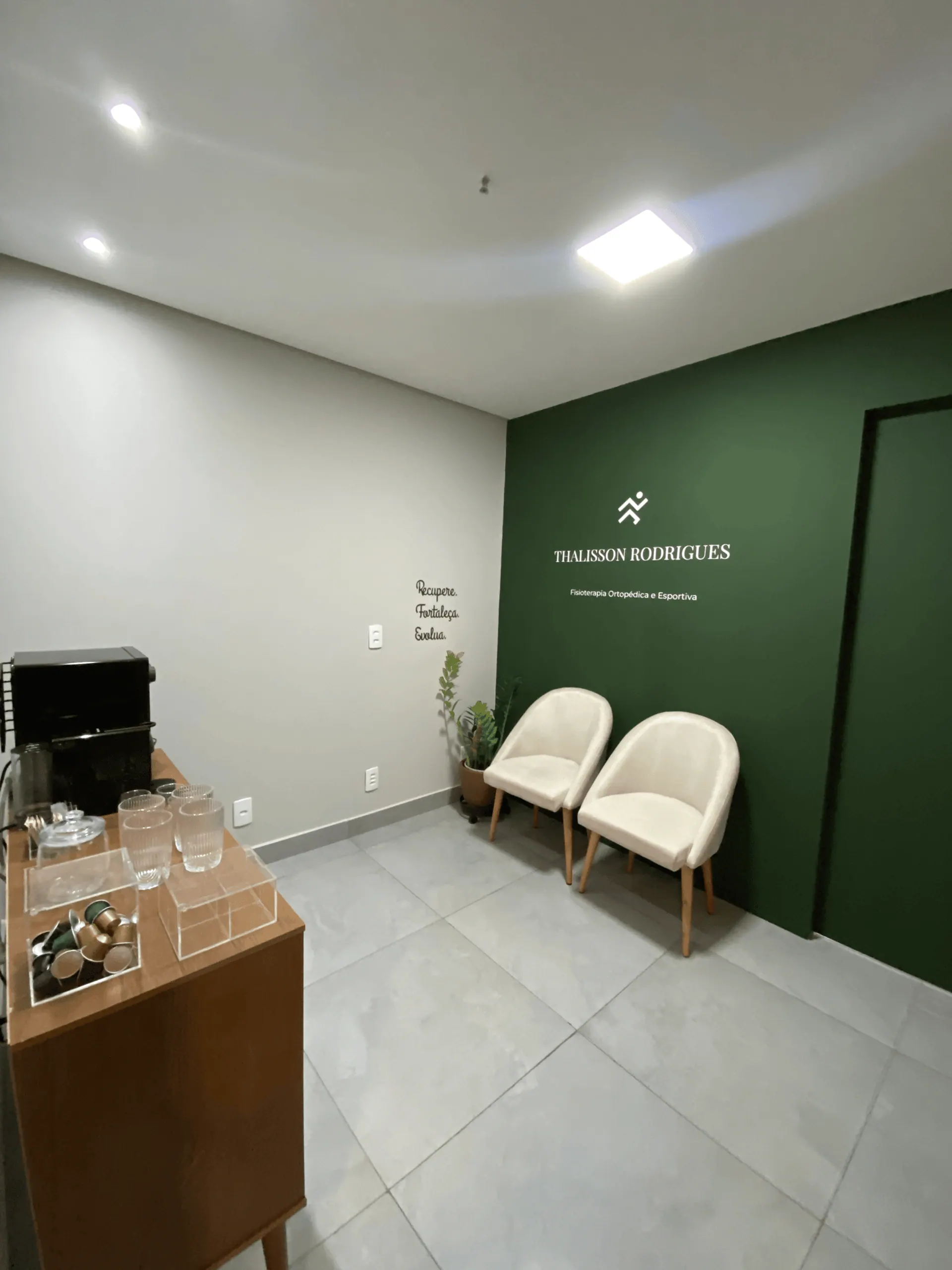 Recepção do Instituto com poltronas claras, plantas e parede verde com a marca